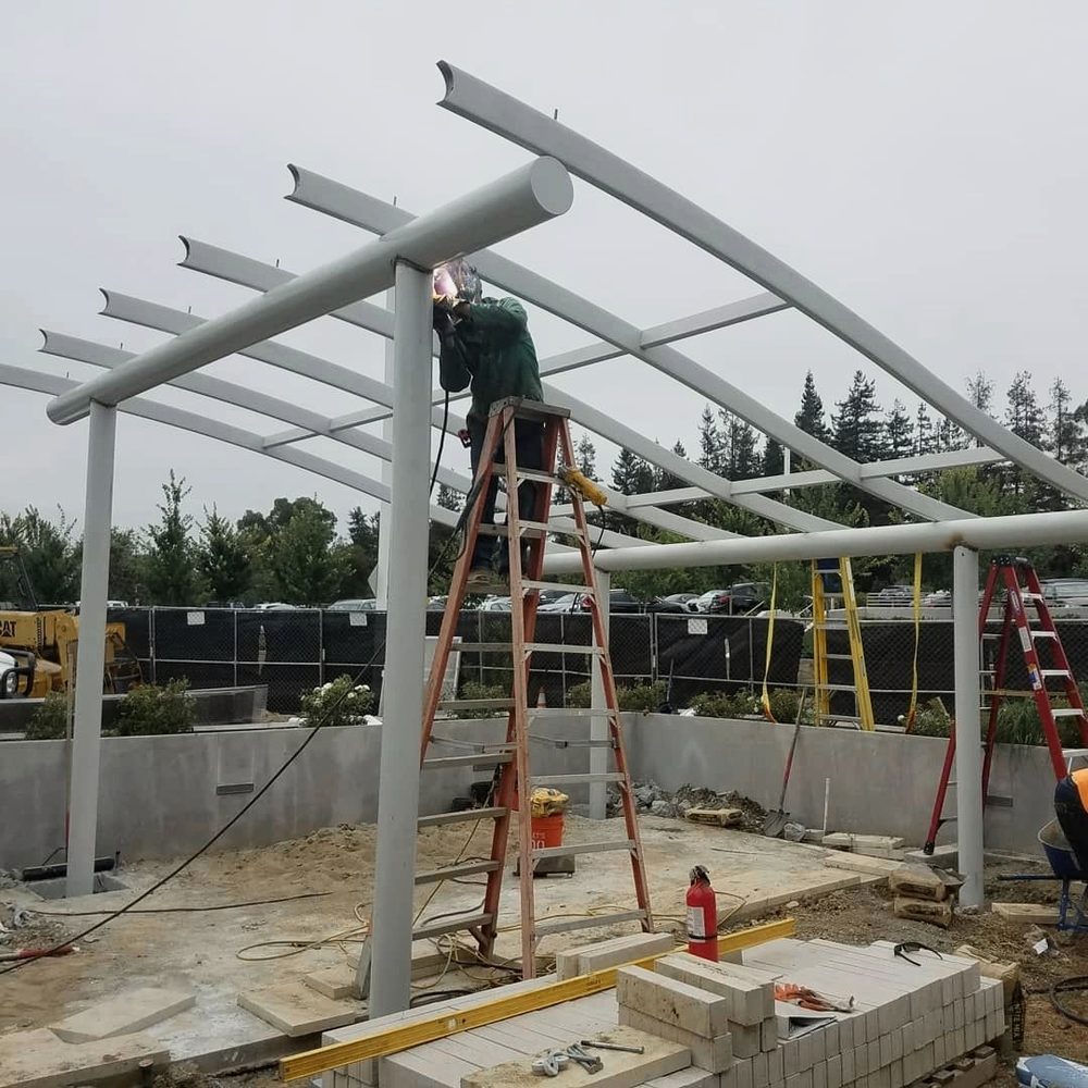 Welder on a ladder joining a steel shade structure frame