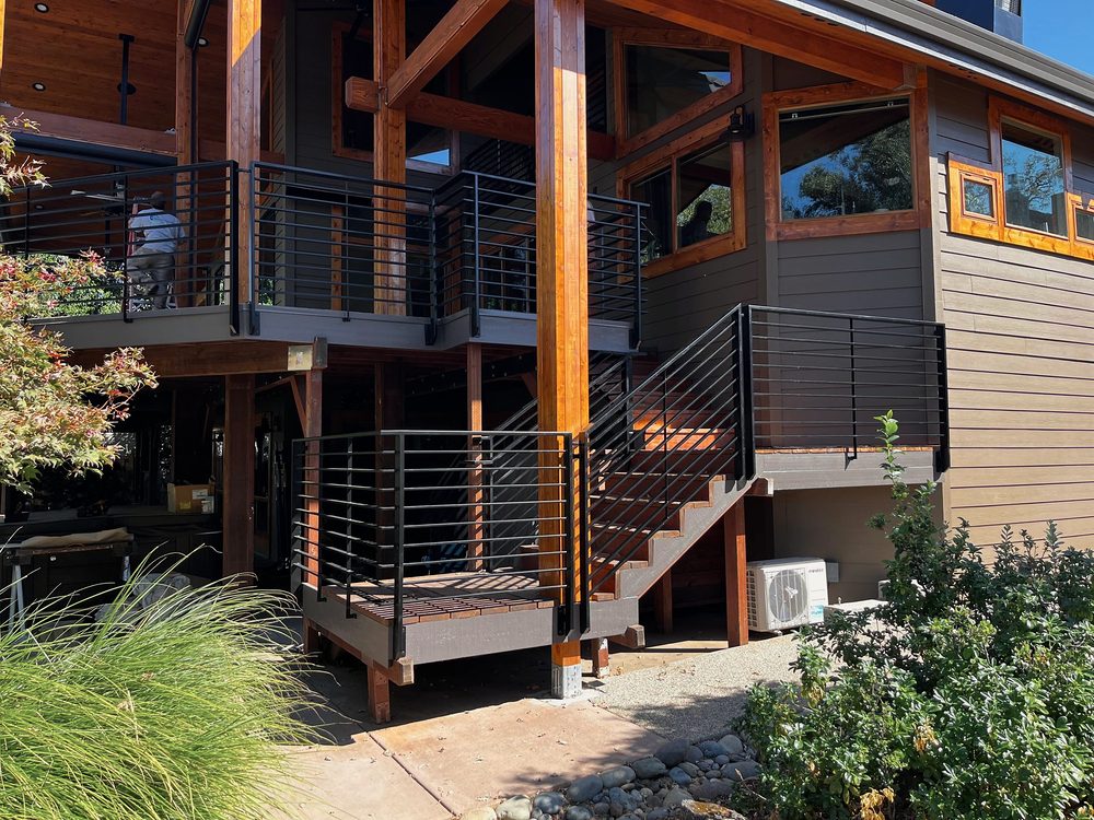 Two-story mountain home with steel-framed exterior stair and black horizontal-bar railings, timber posts