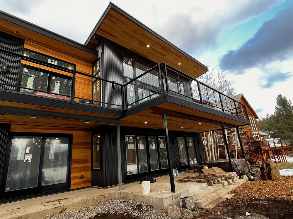 Modern home with cedar and black siding, wraparound black steel balcony railing, dramatic sky