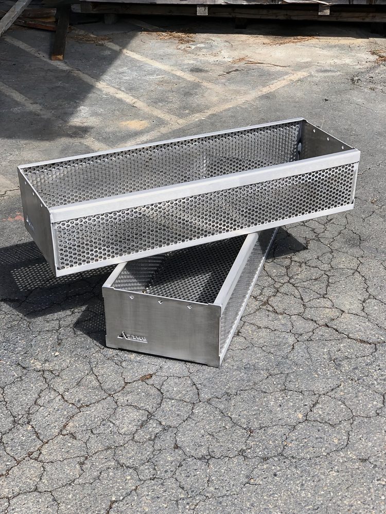 Two stainless perforated-steel trays (one inside the other) on cracked asphalt