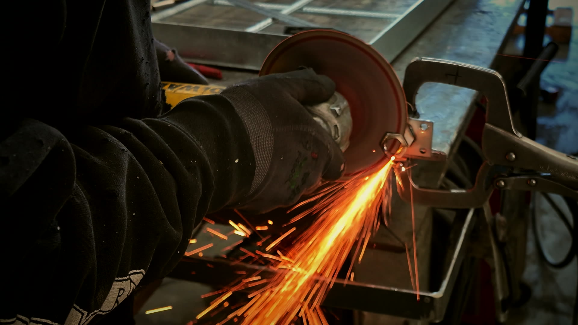 Angle grinder throwing sparks off a steel bracket clamped to a welding table